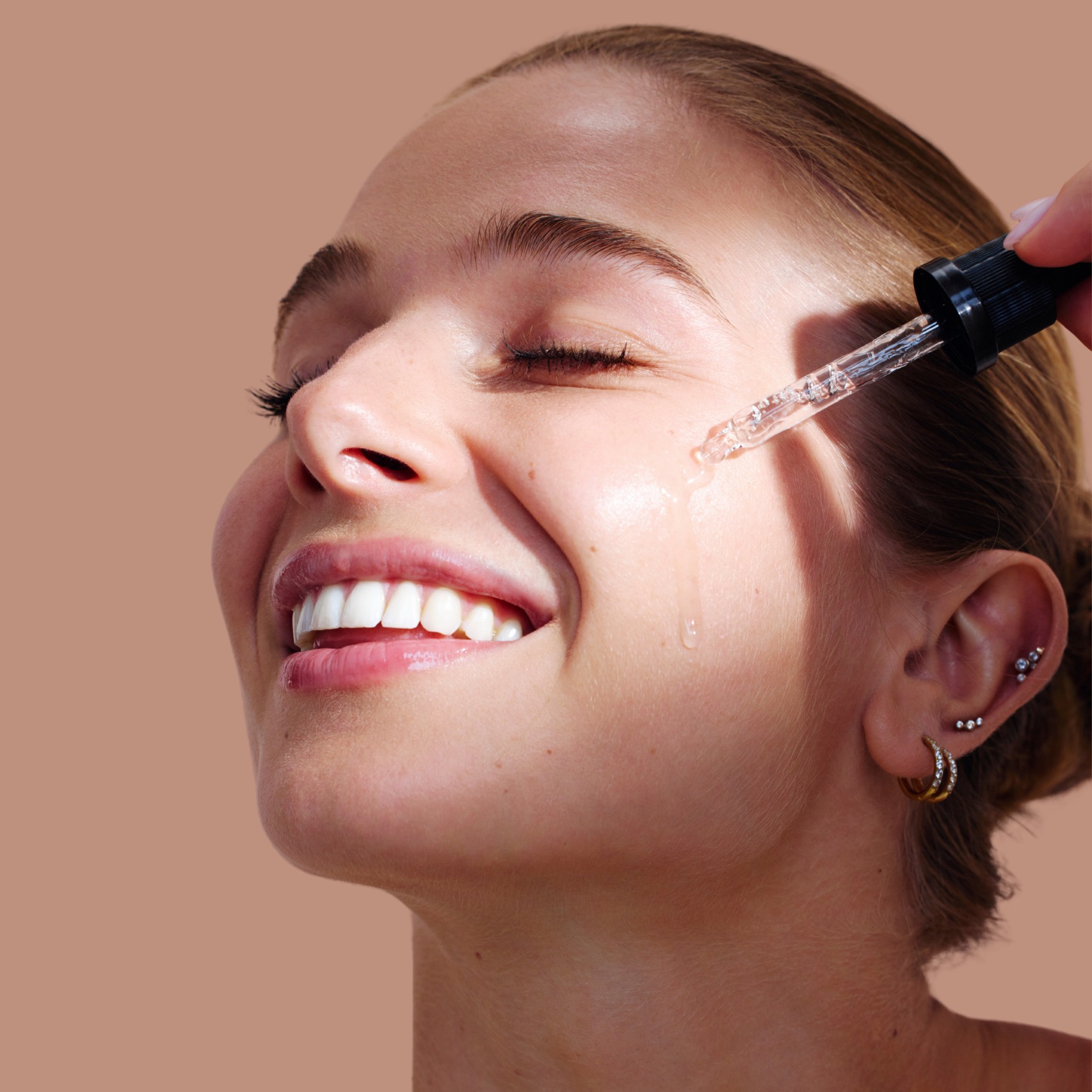 Smiling person applying serum to face with a dropper.