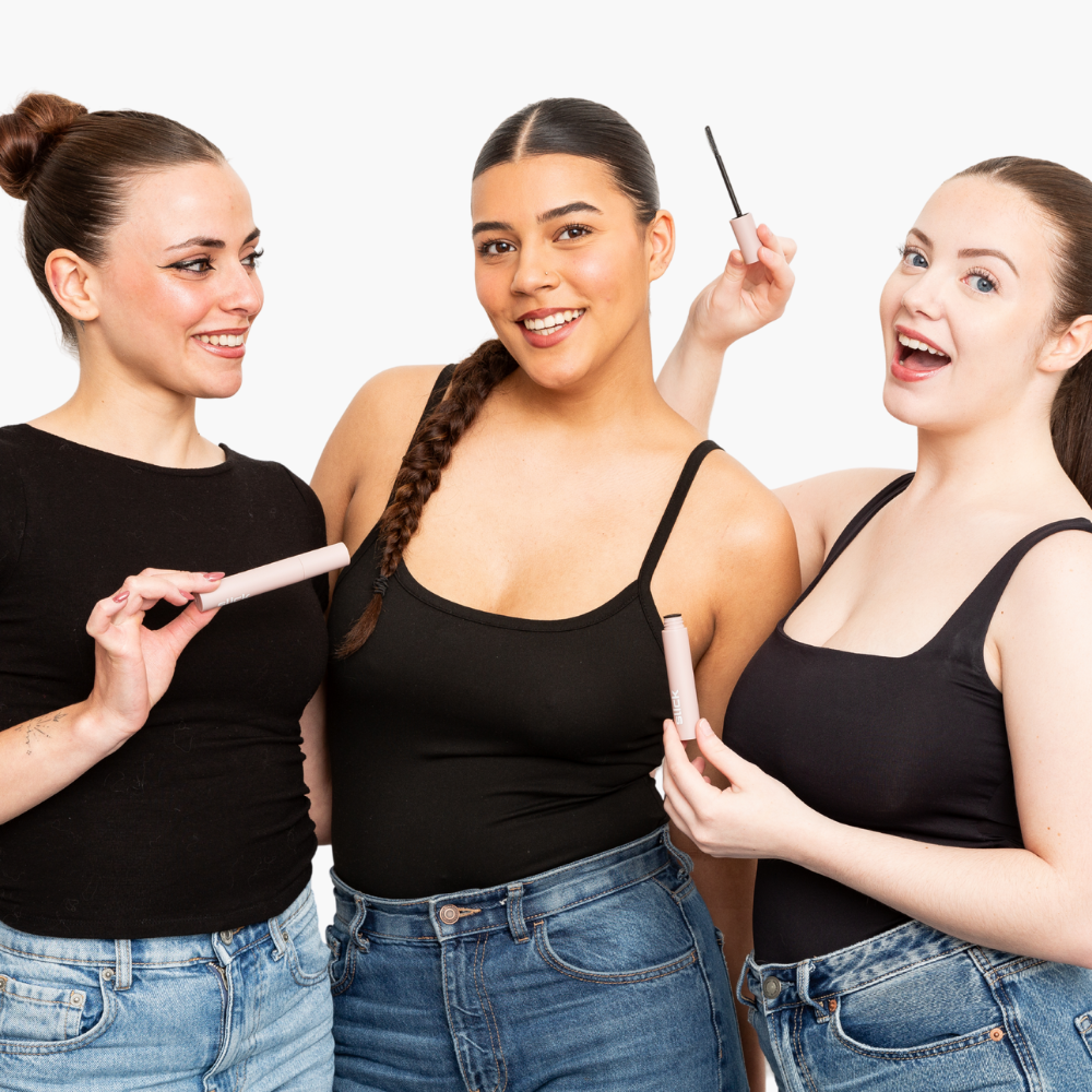 Three women smiling and holding mascara tubes against a white background.