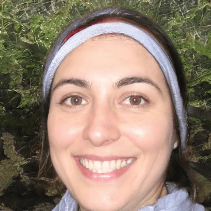 Smiling person with a headband, outdoors with greenery in the background.