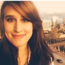 Smiling person with long hair, cityscape in the background.