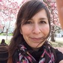 Person smiling in front of blooming cherry blossom trees.