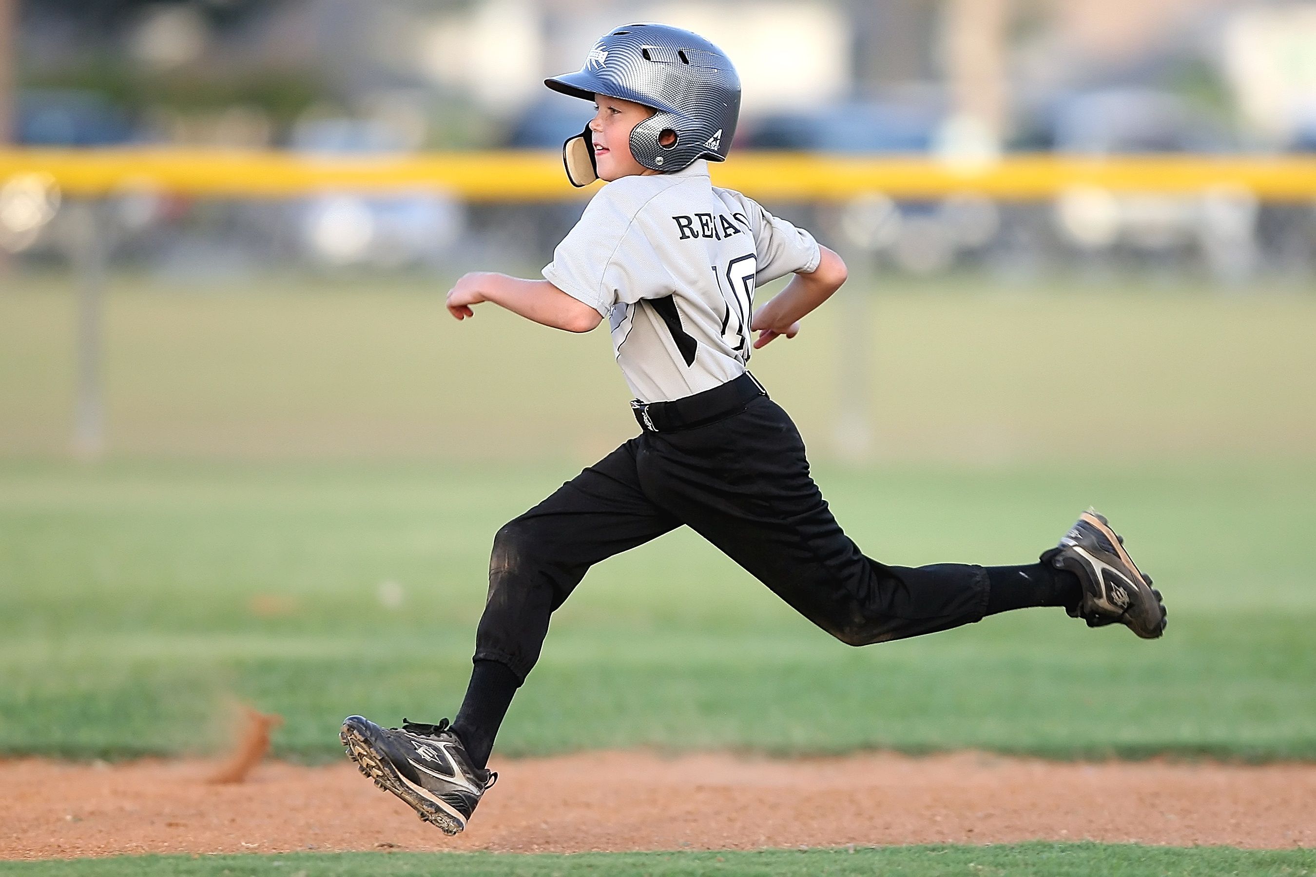A young boy in a baseball uniform and helmet runs across the dirt on a baseball field.
