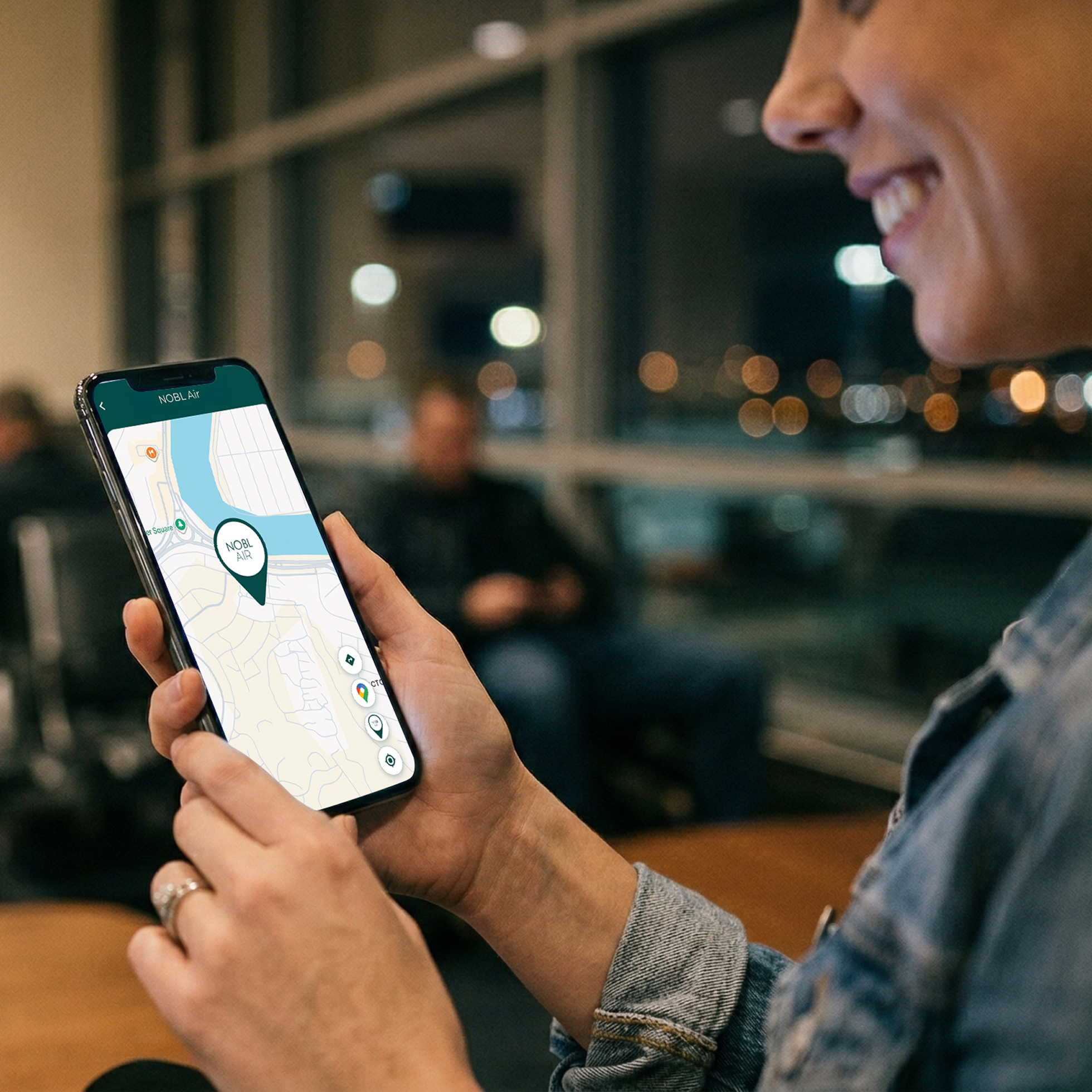 A smiling person looking at a map application on a smartphone in a waiting area at night.