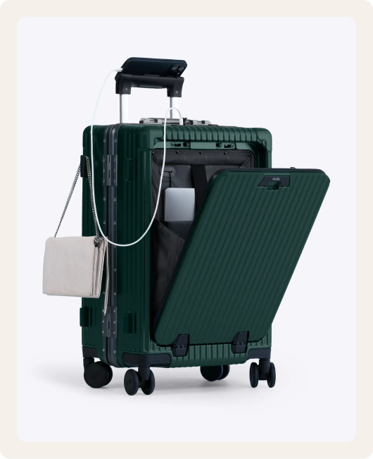 A dark green carry-on suitcase with an open front pocket, charging a phone on its handle.