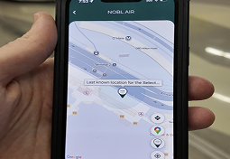 A hand holds a smartphone displaying a location-tracking map app on its screen.
