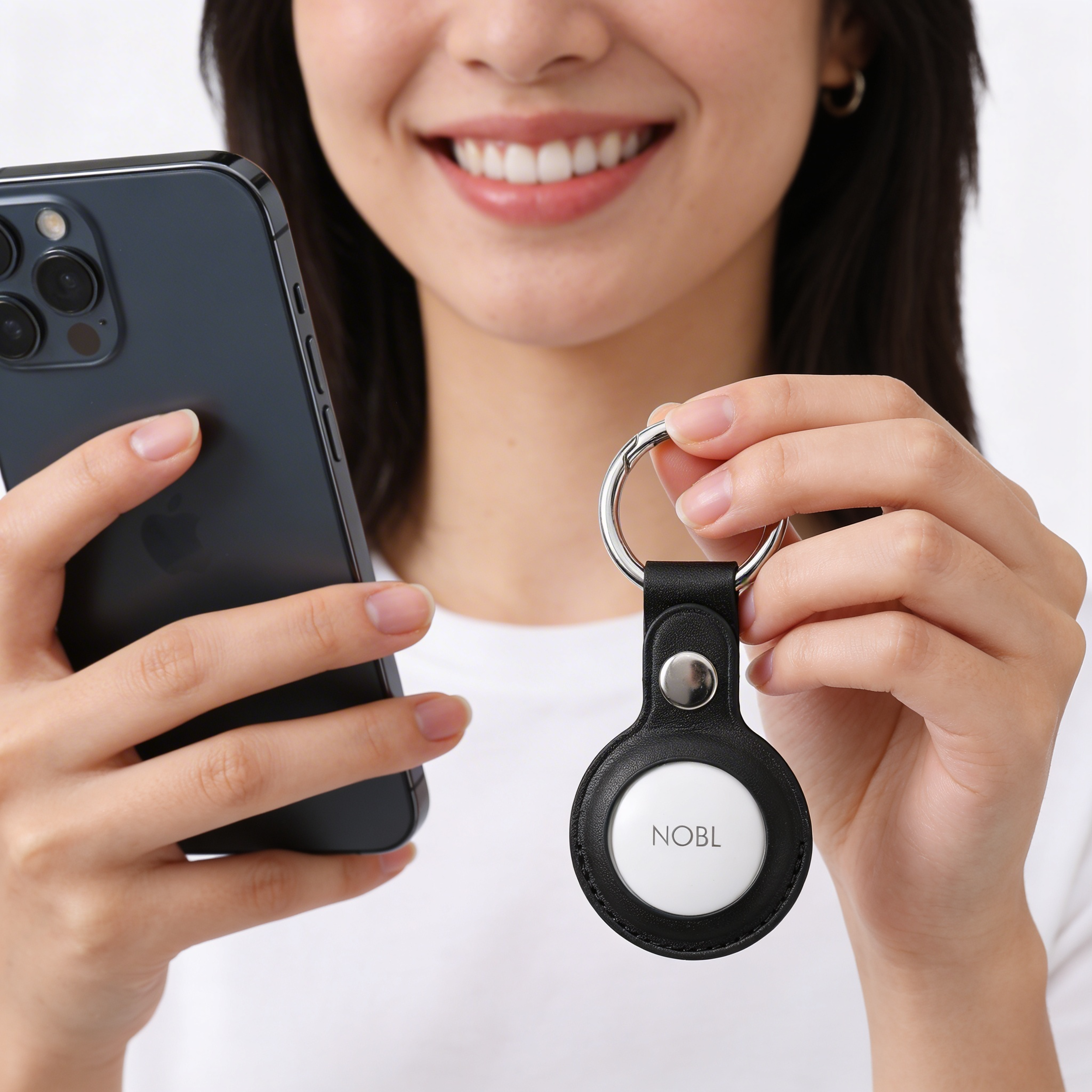 A smiling woman holds a smartphone and a keychain with a NOBL tracking device.