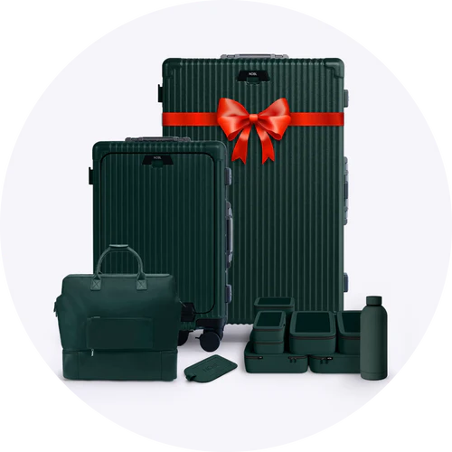 A collection of dark green luggage and travel accessories, with a red bow on the largest suitcase.