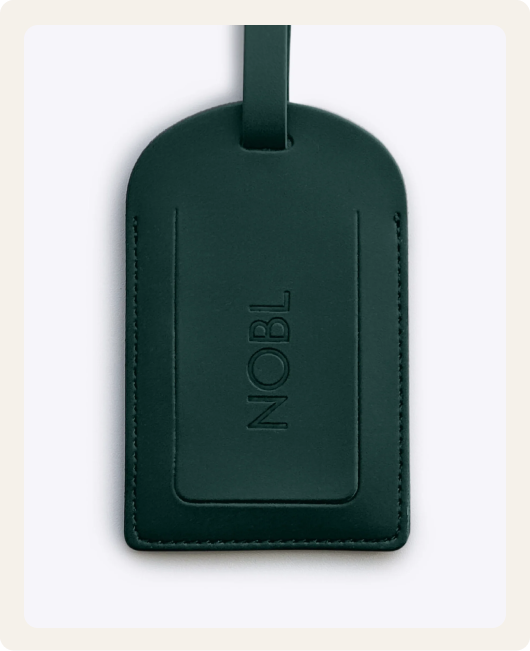 A dark green leather luggage tag with the word 'NOBL' debossed on the front against a light background.