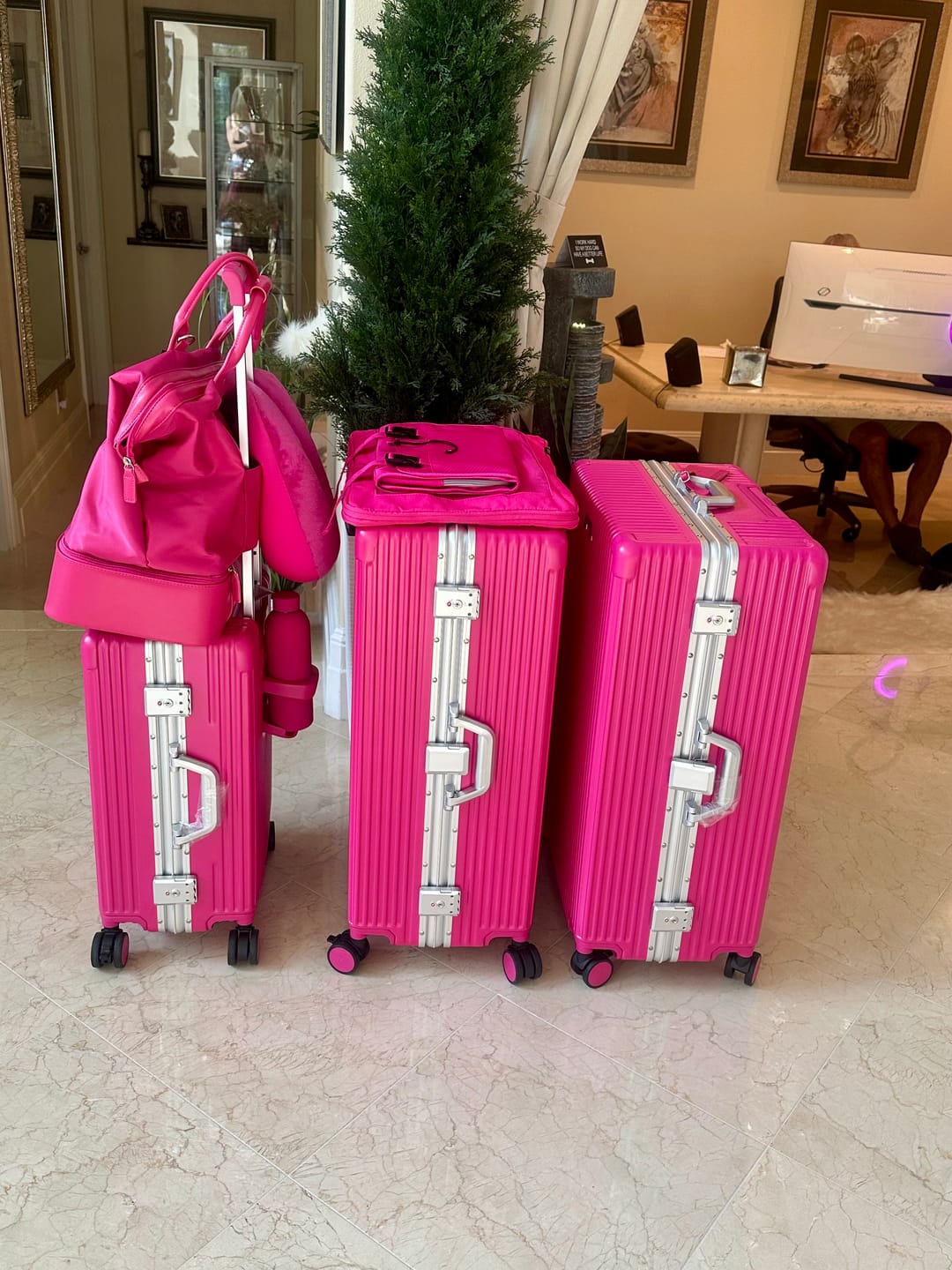Three pink suitcases and a bag next to a small potted tree indoors.