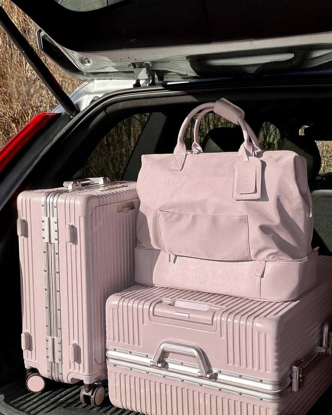 A matching set of pink suitcases and a duffel bag packed in the trunk of a car.