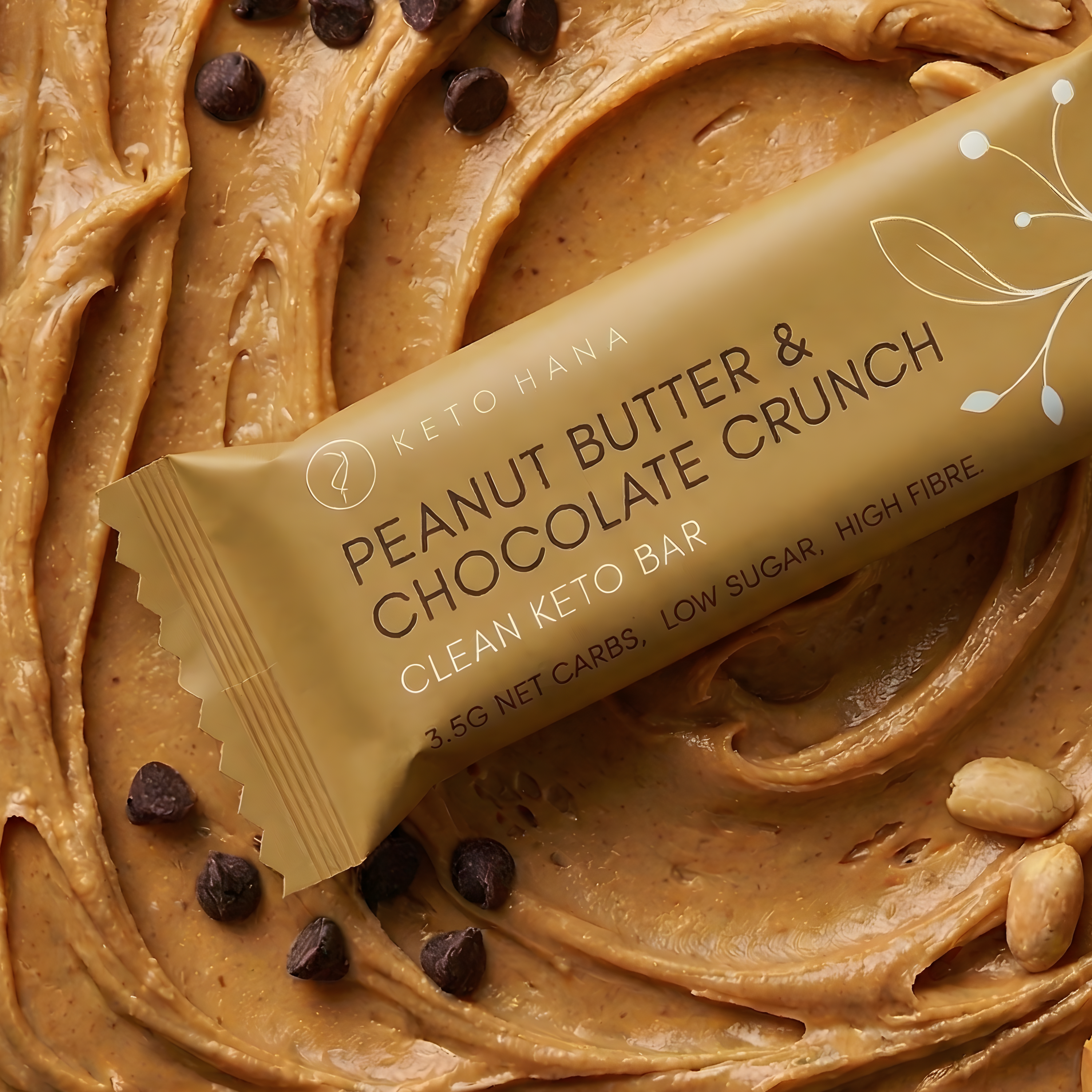 A Keto Hana Peanut Butter & Chocolate Crunch bar resting on swirled peanut butter with chocolate chips.