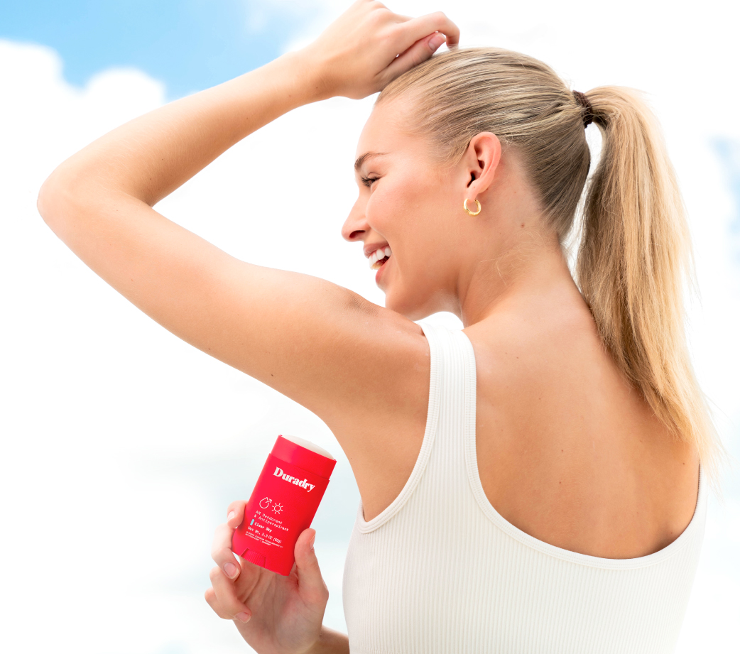 Person holding a red deodorant stick, smiling, with a blue sky background.