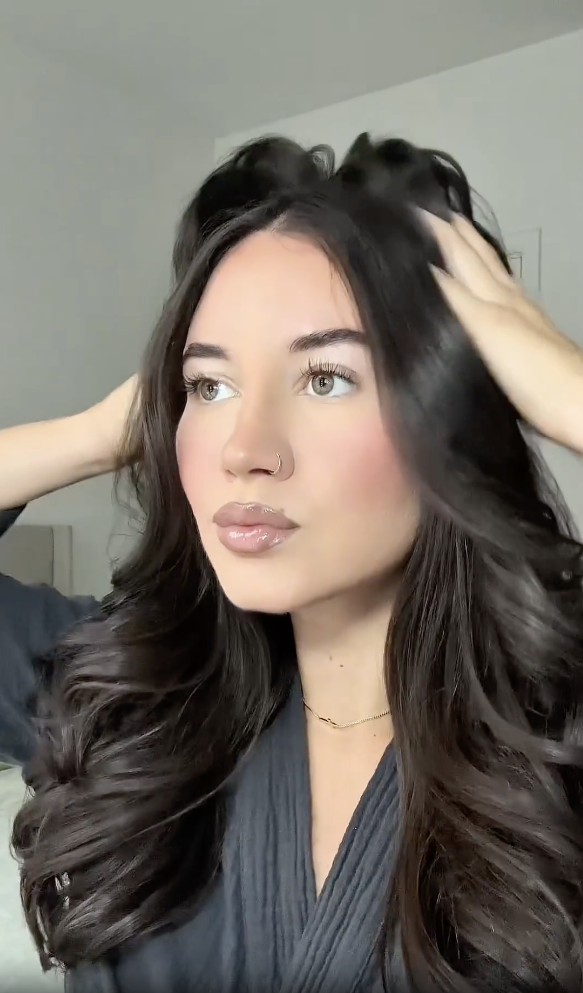 A woman with long, dark, wavy hair runs her hands through it while looking to the side.