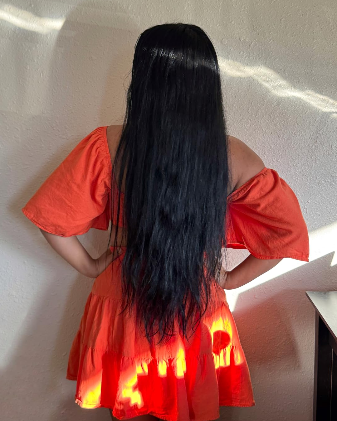 Back view of a person with very long black hair wearing a bright orange dress.