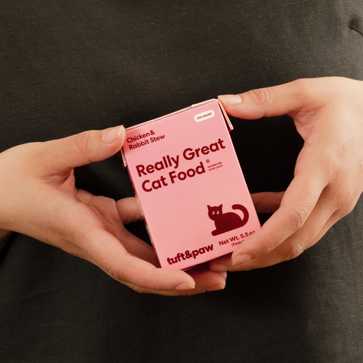 A person holds a pink box of tuft & paw Really Great Cat Food in their hands.