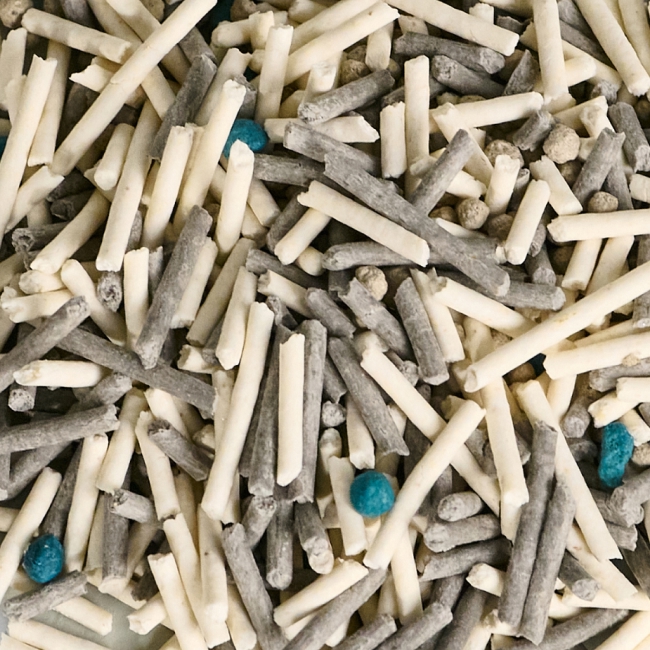 A close-up of grey, off-white, and blue cat litter pellets and granules.