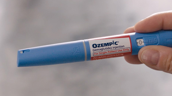 A hand holding a blue Ozempic injection pen.