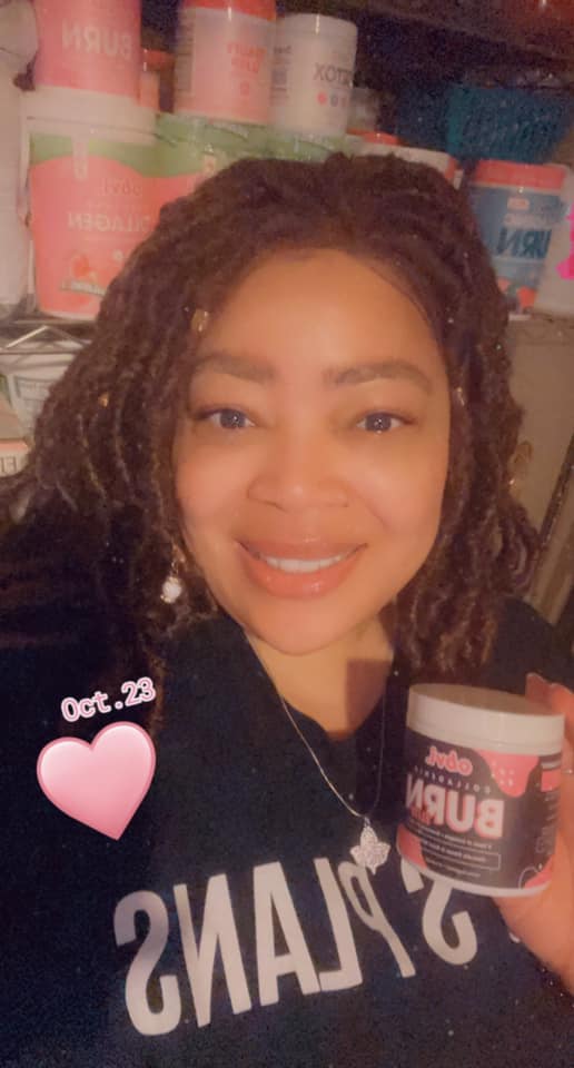 Smiling person holding a jar in front of shelves filled with various products.