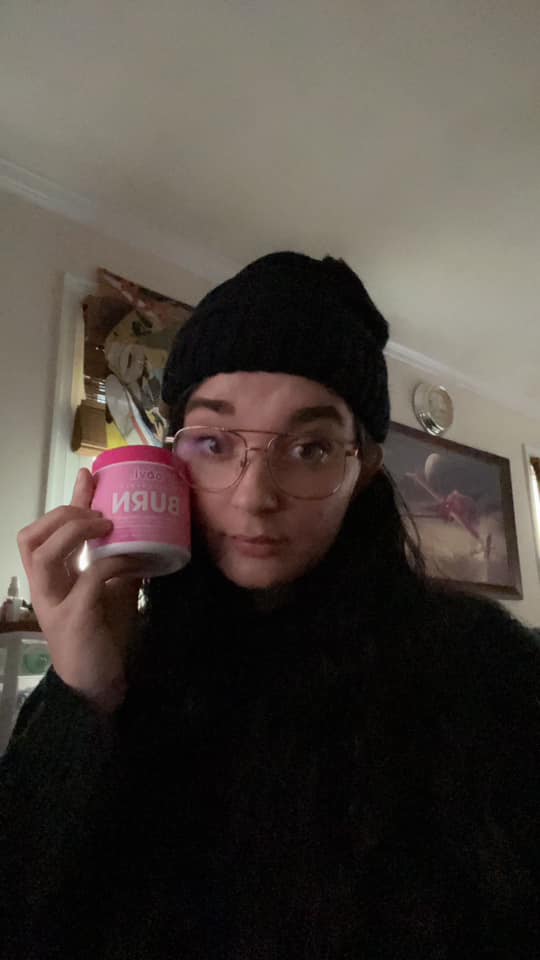 Person wearing glasses and a hat, holding a container labeled 'BURN'.