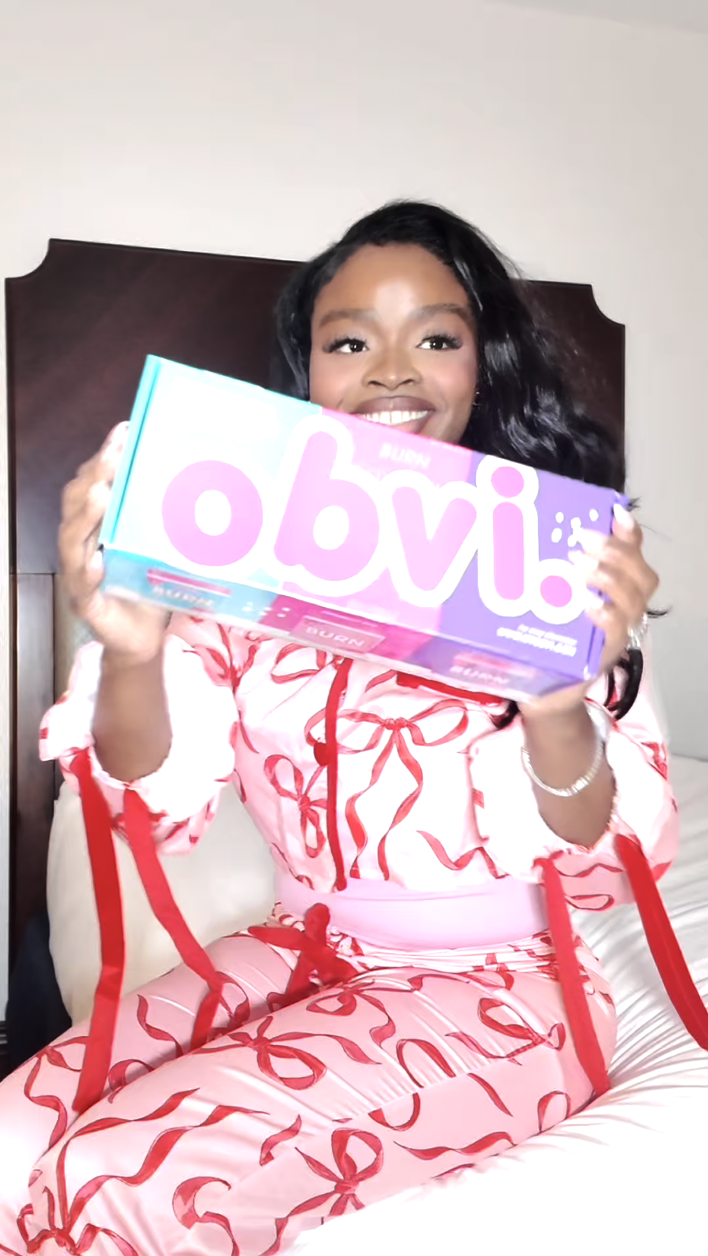 Person holding a colorful box labeled 'obvi.' while sitting on a bed.