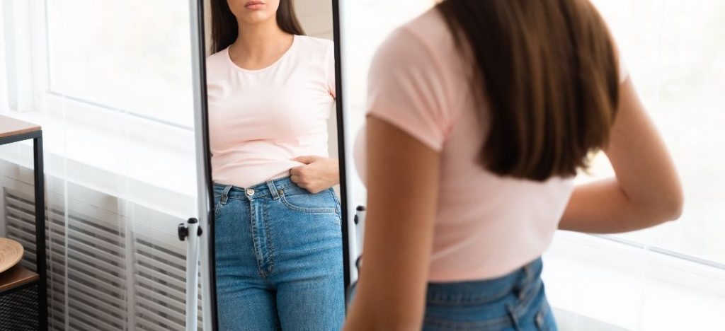 Woman looking at her reflection in a full-length mirror, adjusting her jeans.