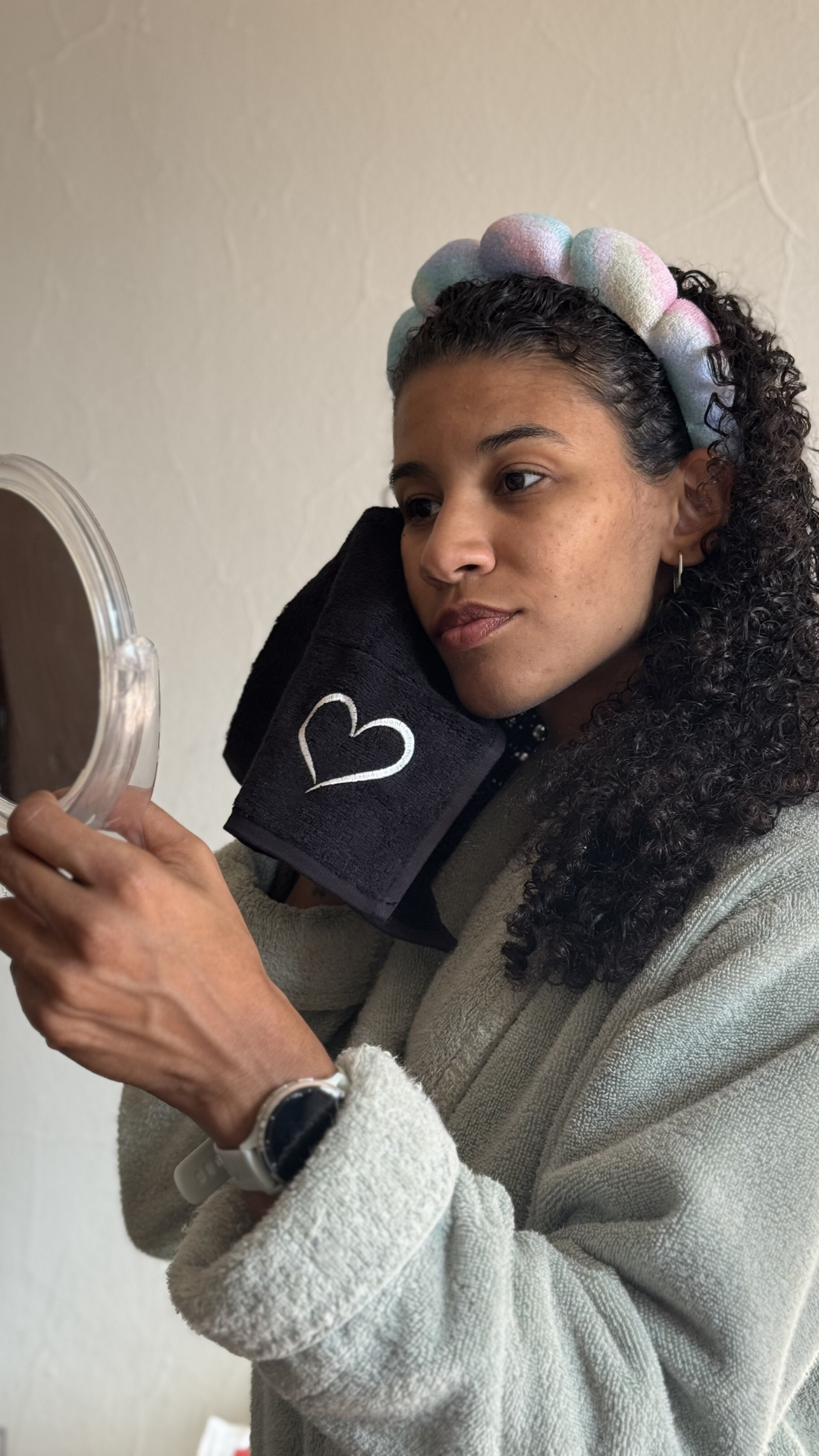 Person with headband uses a black towel while looking in a handheld mirror.