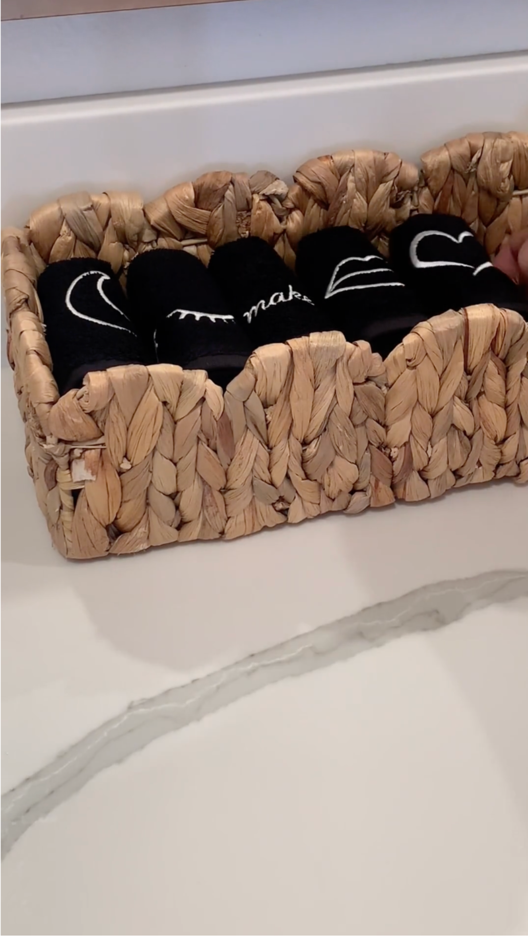 A woven basket on a counter holding rolled black cloths with white embroidery.