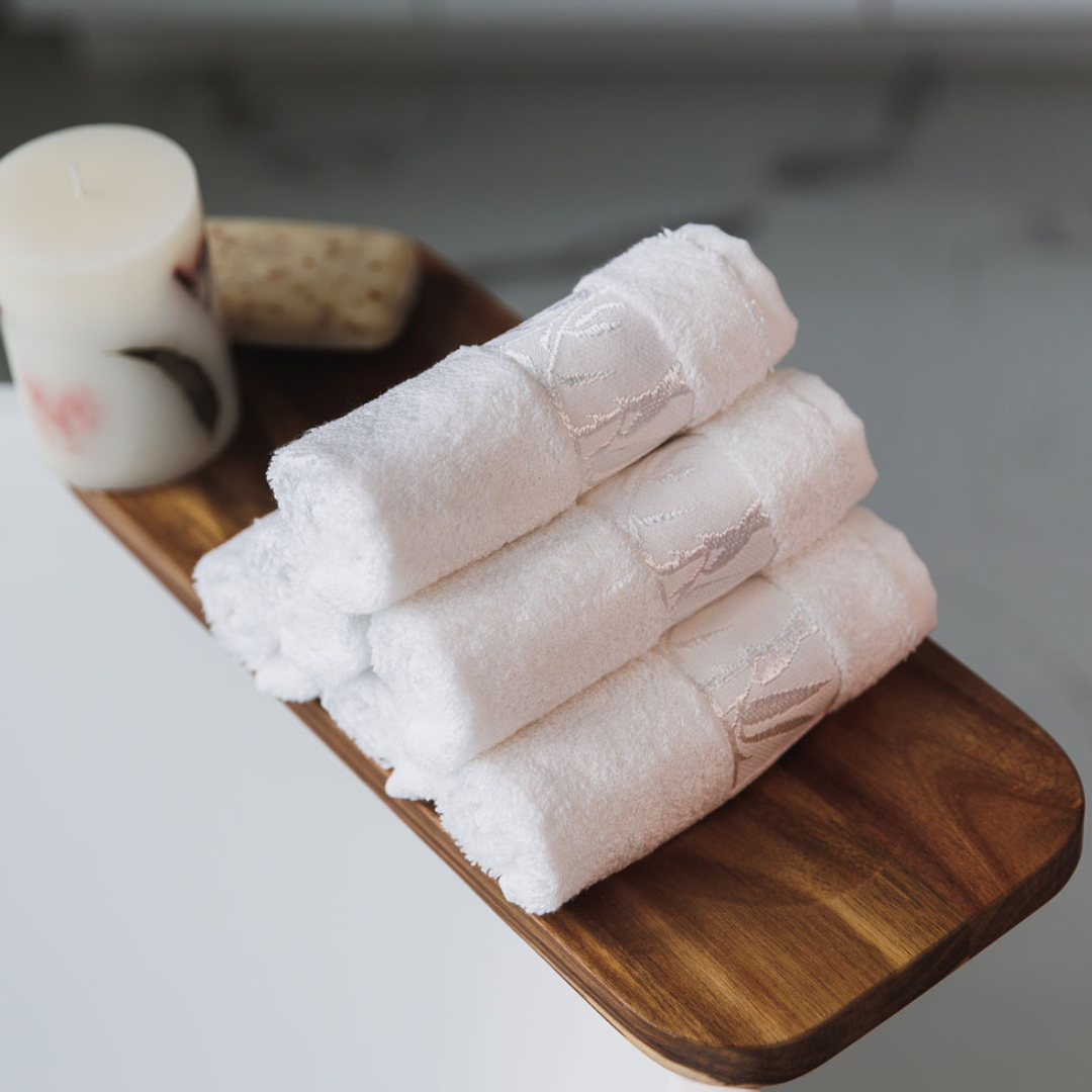Stack of white towels on a wooden tray with a candle nearby.