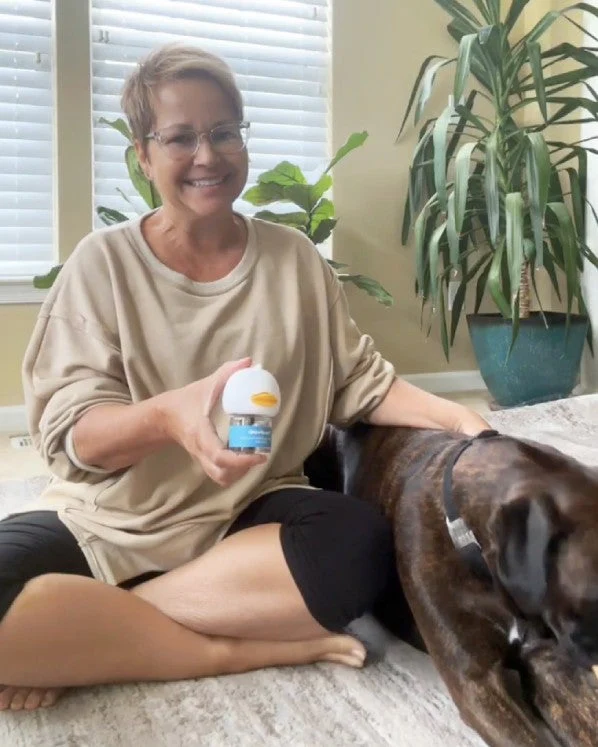 Person sitting indoors with a dog, holding a small container.