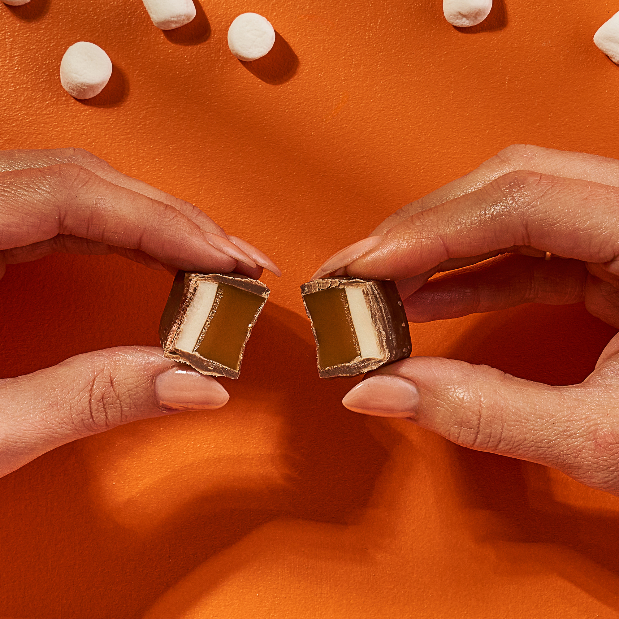 Two hands holding a split chocolate candy against an orange background.