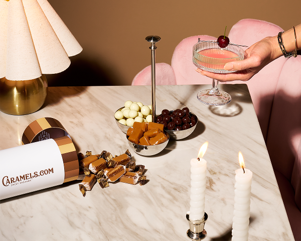 A marble table with sweets, candles, lamp, and a hand holding a cocktail.