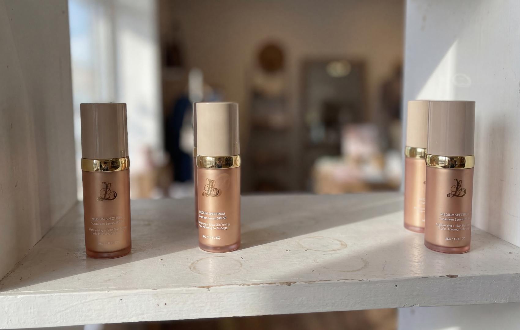 Four cosmetic bottles on a white wooden shelf in a room.