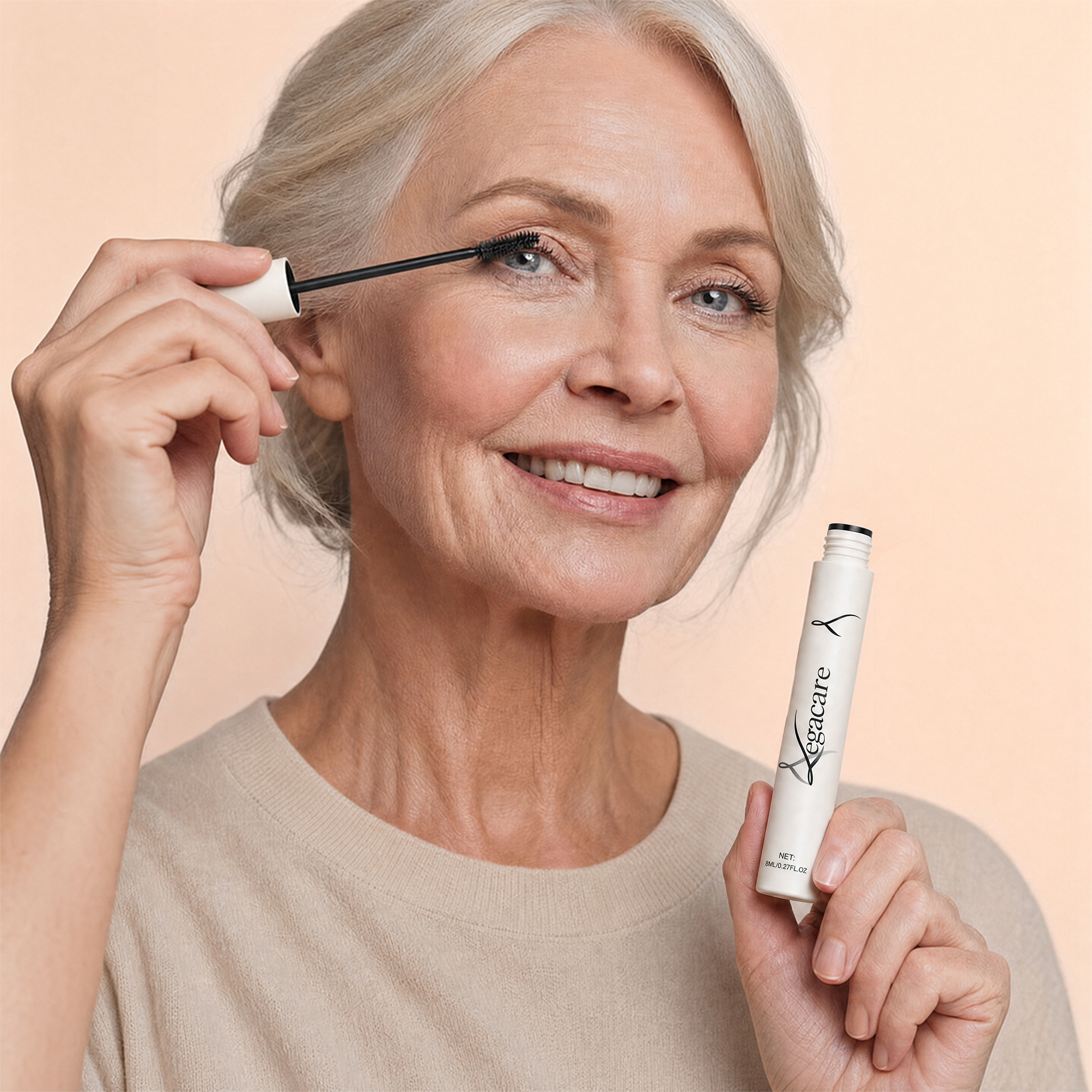 A smiling older woman with grey hair applies mascara to her eyelashes while holding the mascara tube.