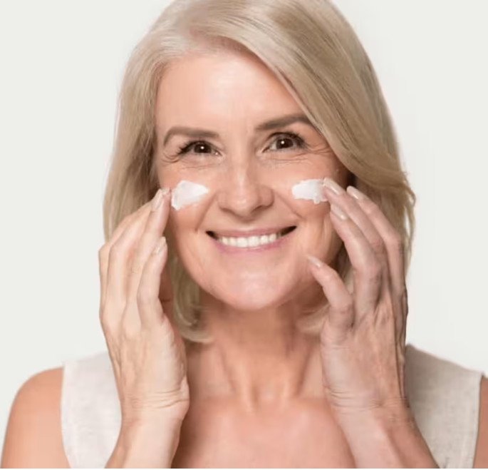 Smiling woman applying cream to her cheeks.