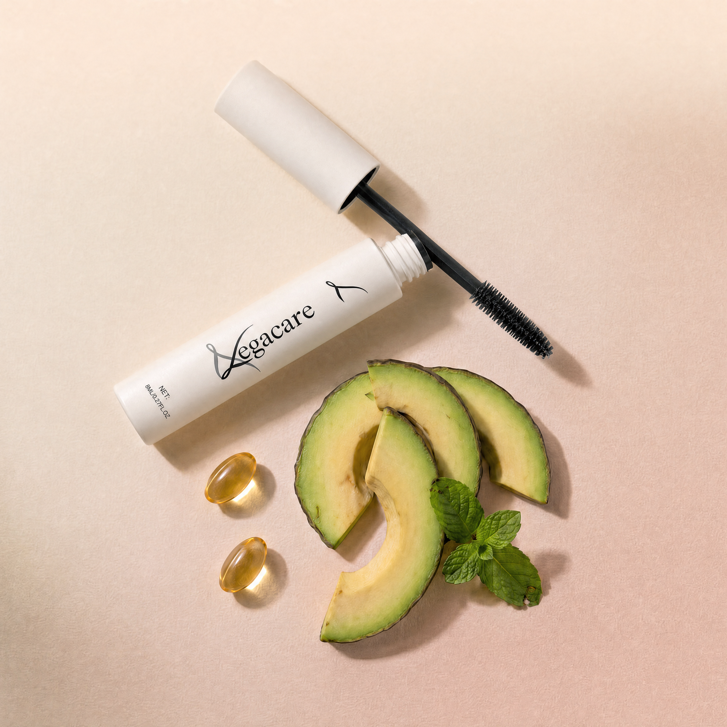 An open tube of Vegacare mascara next to avocado slices, mint, and two golden capsules.