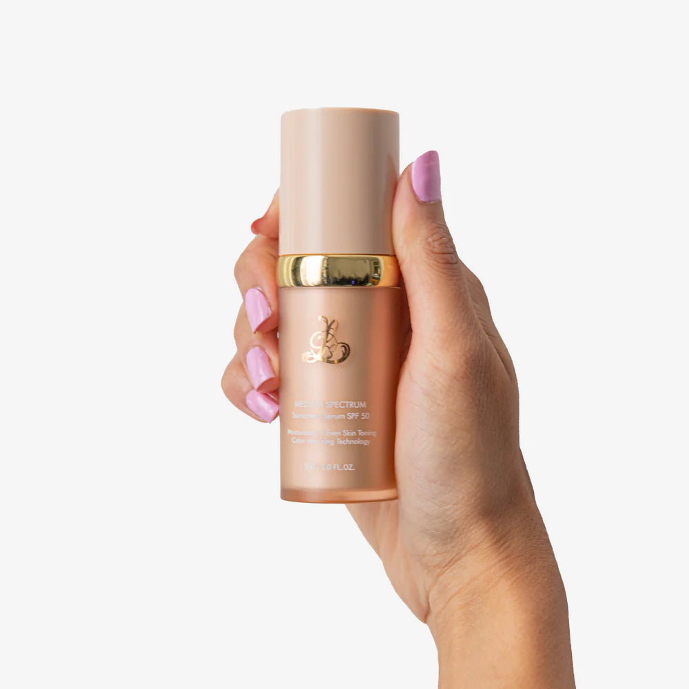 Hand holding a beige cosmetic bottle with gold accents.