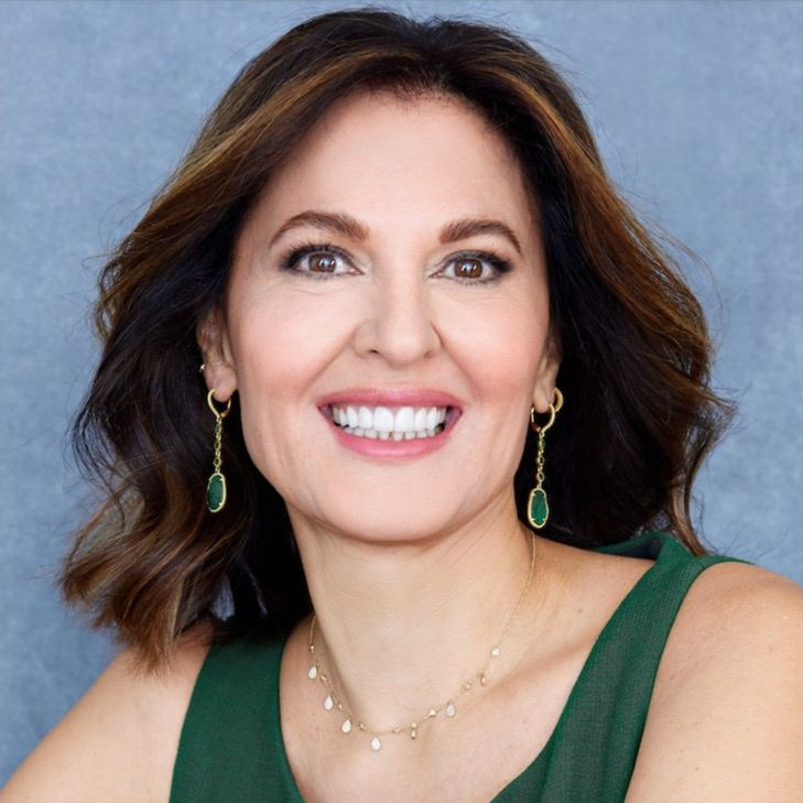 Smiling woman with shoulder-length brown hair wearing green earrings and a green top.