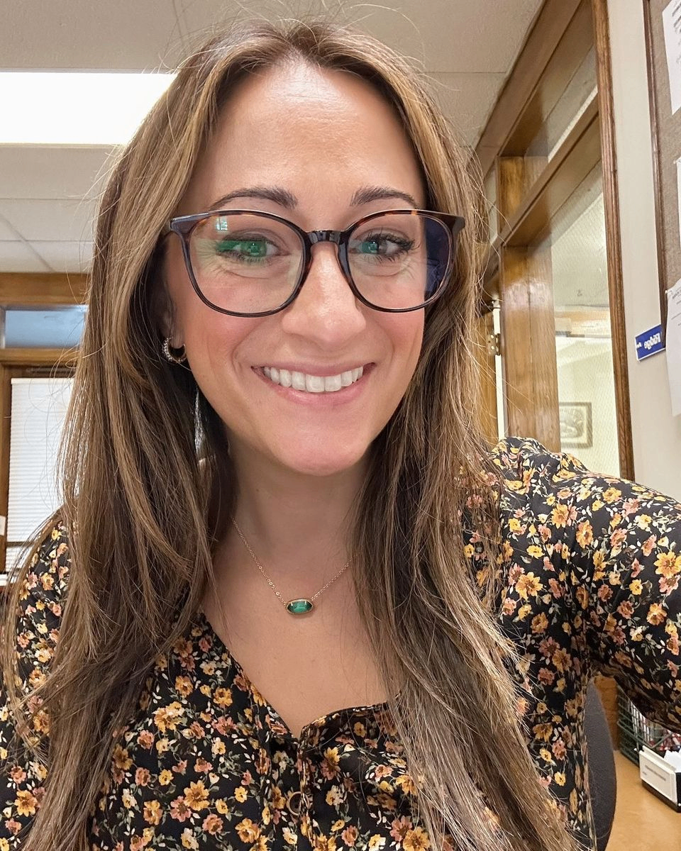 Person smiling in an office wearing glasses and a floral top.