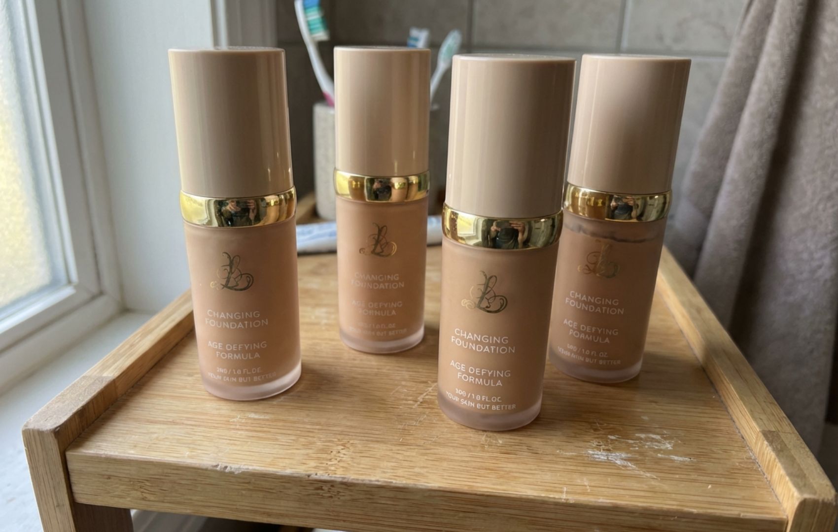 Four bottles of 'Changing Foundation' makeup sitting on a wooden tray in a bathroom.