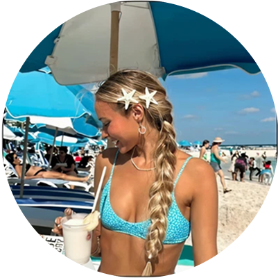 Person in a blue bikini with a drink on a sunny beach.