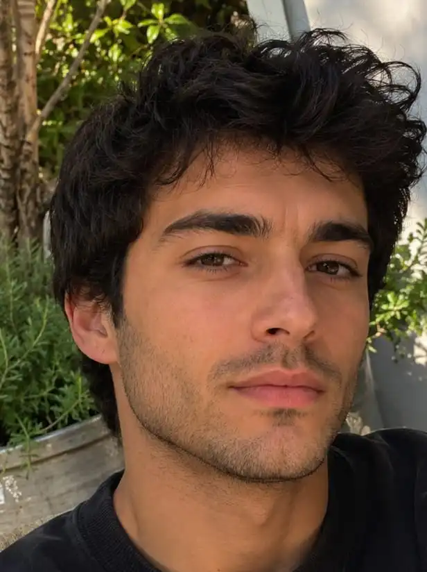 A close-up portrait of a young man with dark, wavy hair and brown eyes, looking at the camera.
