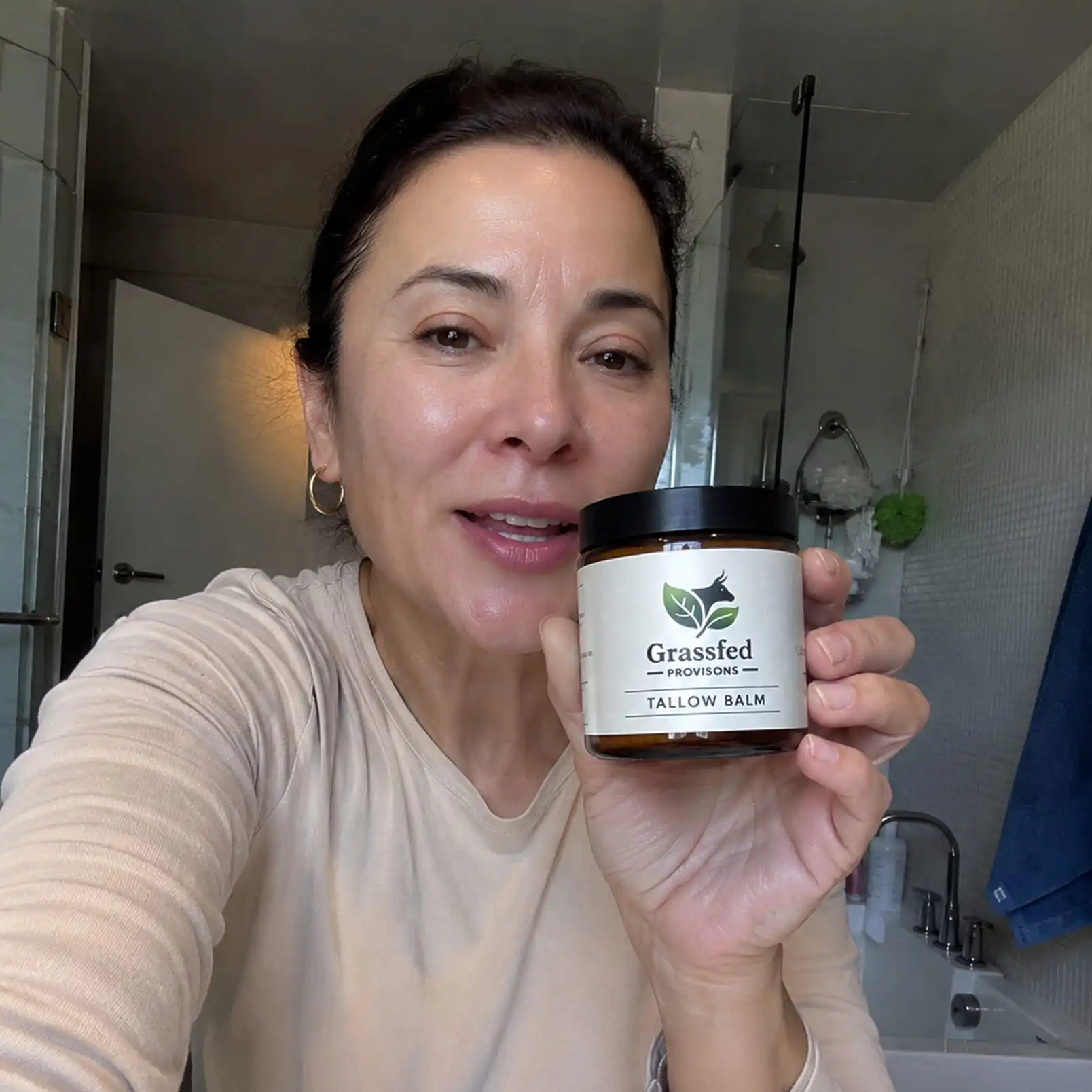 A woman in a bathroom holds up a jar of Grassfed Provisions Tallow Balm.