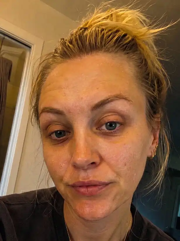 A close-up of a woman with blonde hair pulled into a messy bun, looking into the camera.