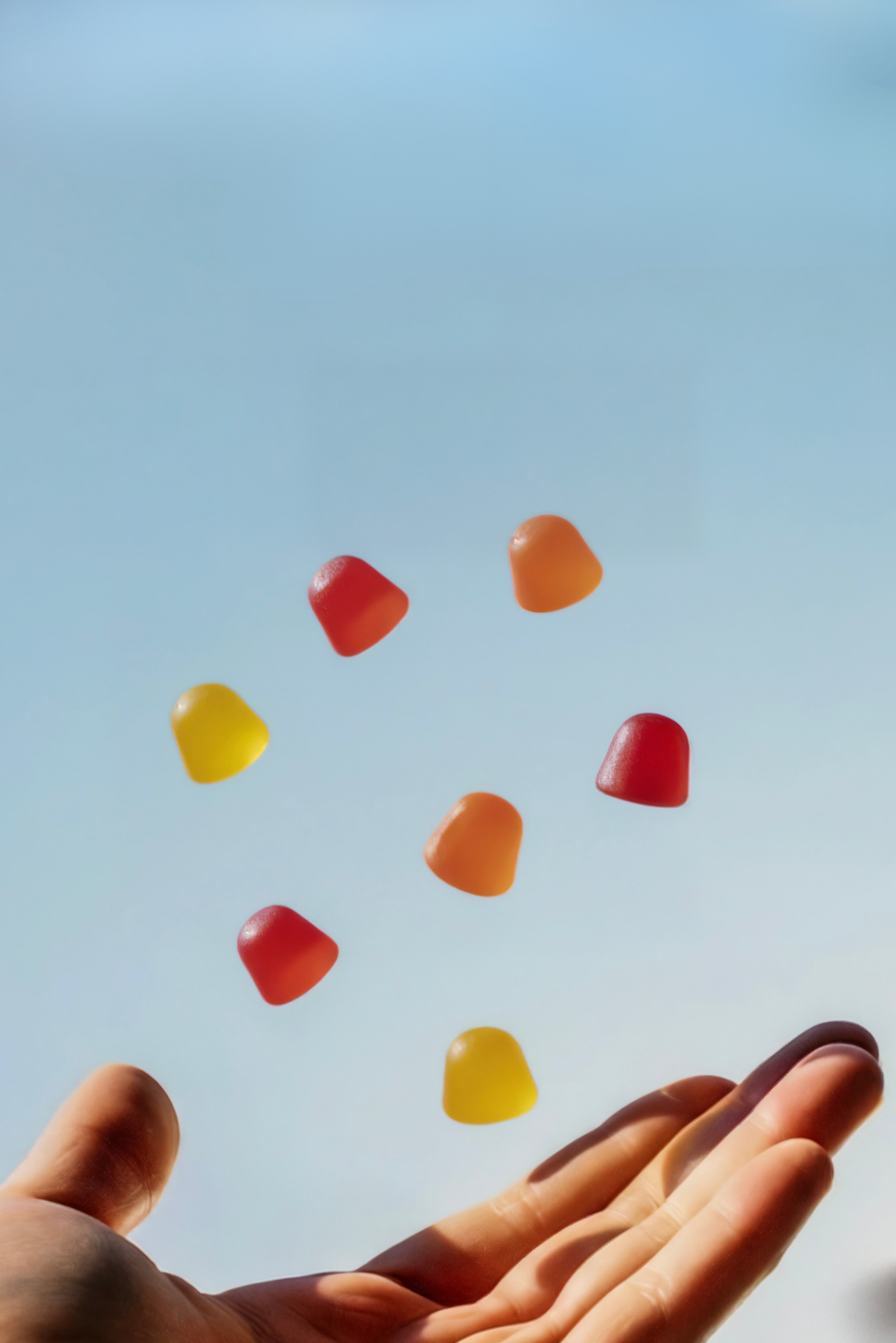 Colorful gummy candies floating above an open hand against a light blue background.