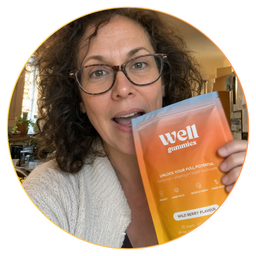 A woman with curly hair and glasses holds up a pouch of Well Gummies with an excited expression.