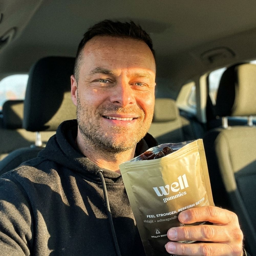 A smiling man in a car holds up a gold-colored pouch of Well gummies.