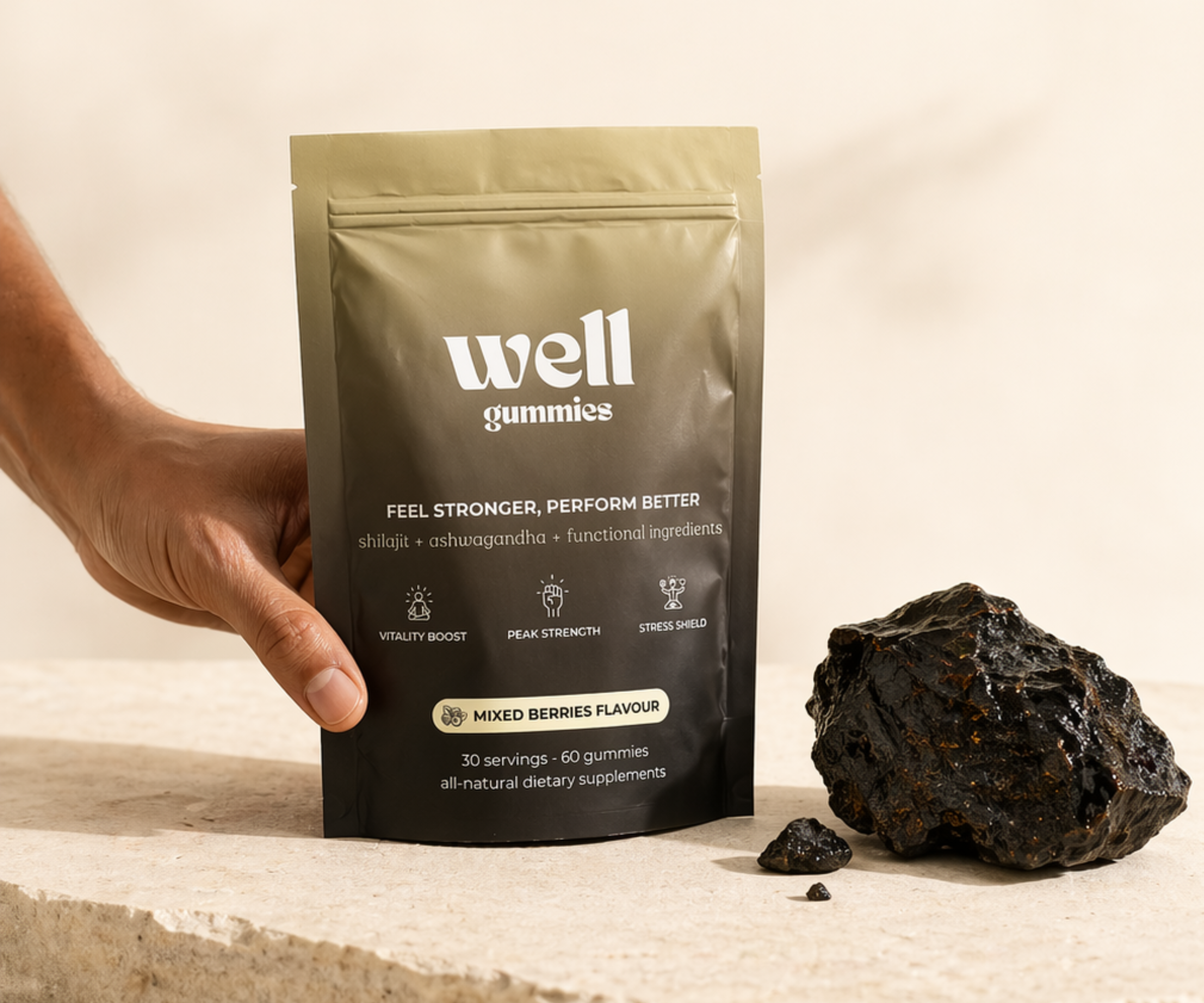 A hand holds a pouch of Well Gummies next to a large piece of shilajit resin.