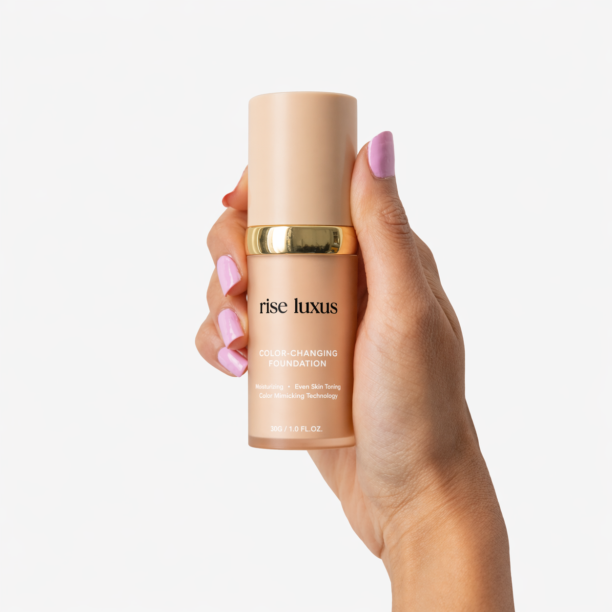 A hand with purple nails holds a beige bottle of Rise Luxus Color-Changing Foundation against a white background.