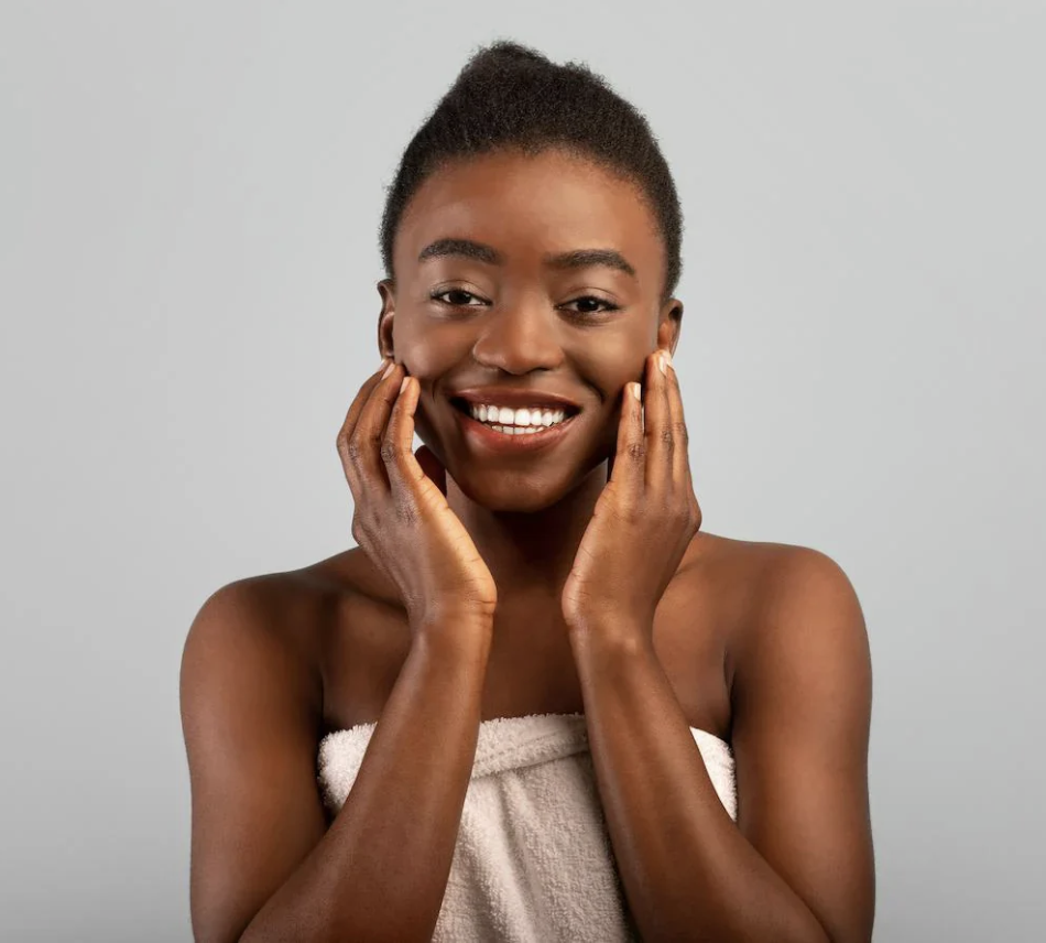 Smiling person wrapped in a towel, touching their face.