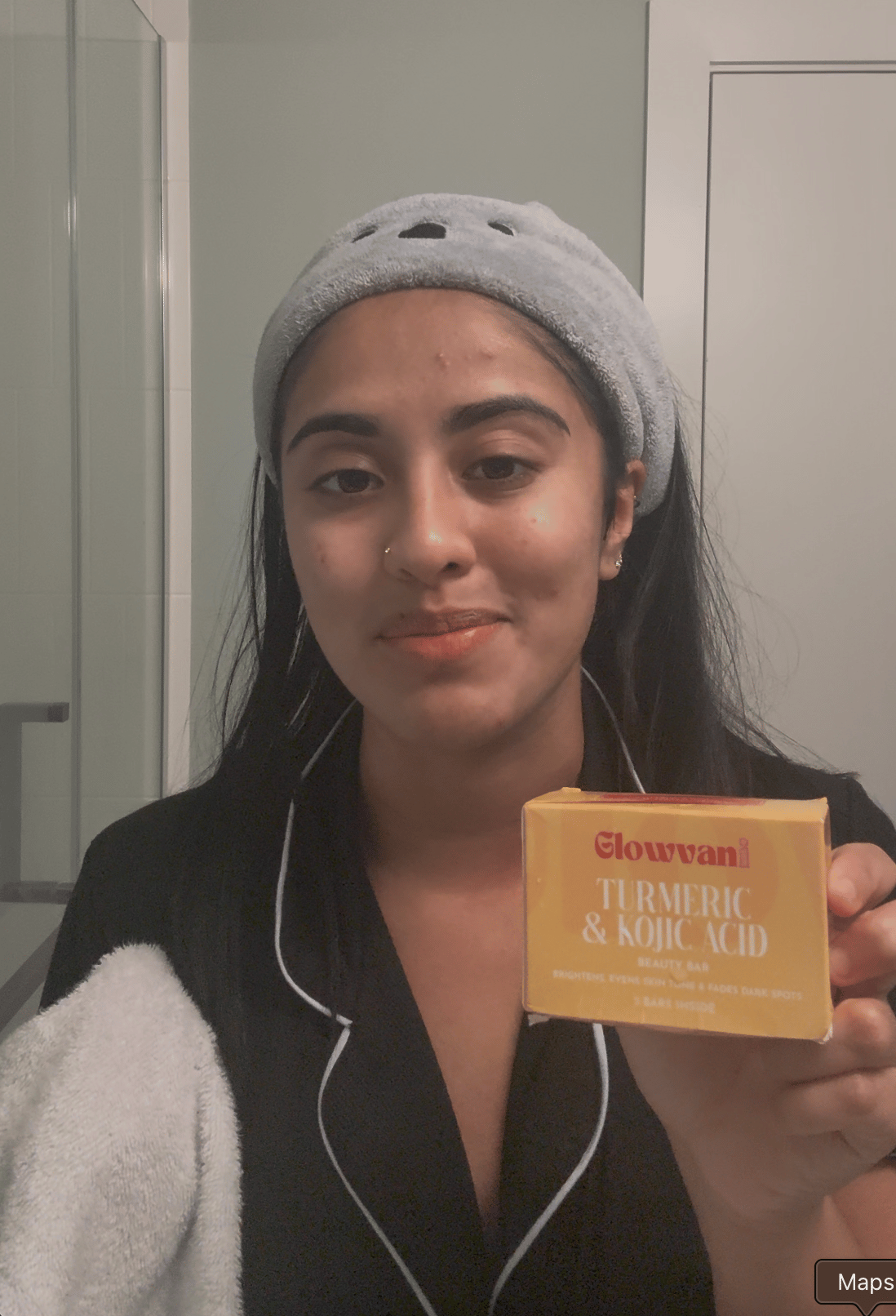 A woman wearing a headband and pajamas holds a white towel and a yellow box of soap.